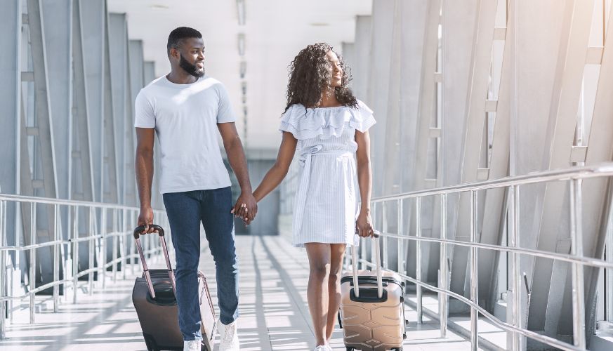 a Black couple smiling and holding hands with suitcases